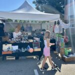 Ein Mädchen läuft an einem bunten Verkaufsstand vorbei, an dem eine Verkäuferin steht.